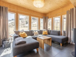 Un salon moderne avec un canapé d’angle, une petite table en bois et de grandes fenêtres donnant sur l’extérieur.