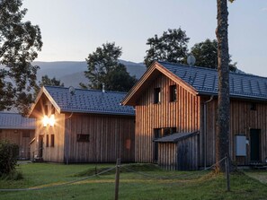 A row of wooden cabins with a metal roof, surrounded by grass and trees, with a mountain in the background. - One-bedroom Cabin (Sankt Georgen am Kreischberg)