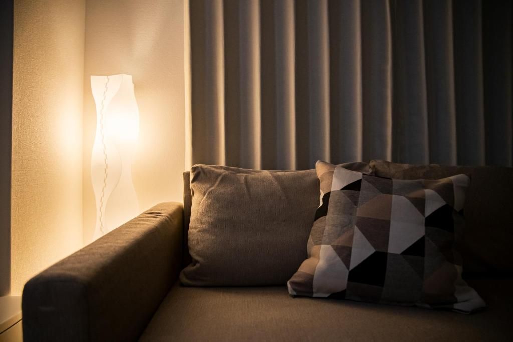 A sofa with two cushions, a wall-mounted lamp, and a window with vertical blinds.