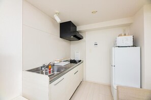 A compact kitchen with a black range hood, a white refrigerator, and a sink with a dish rack. - Presence Hakata (Fukuoka City Hakata-ku Chiyo)