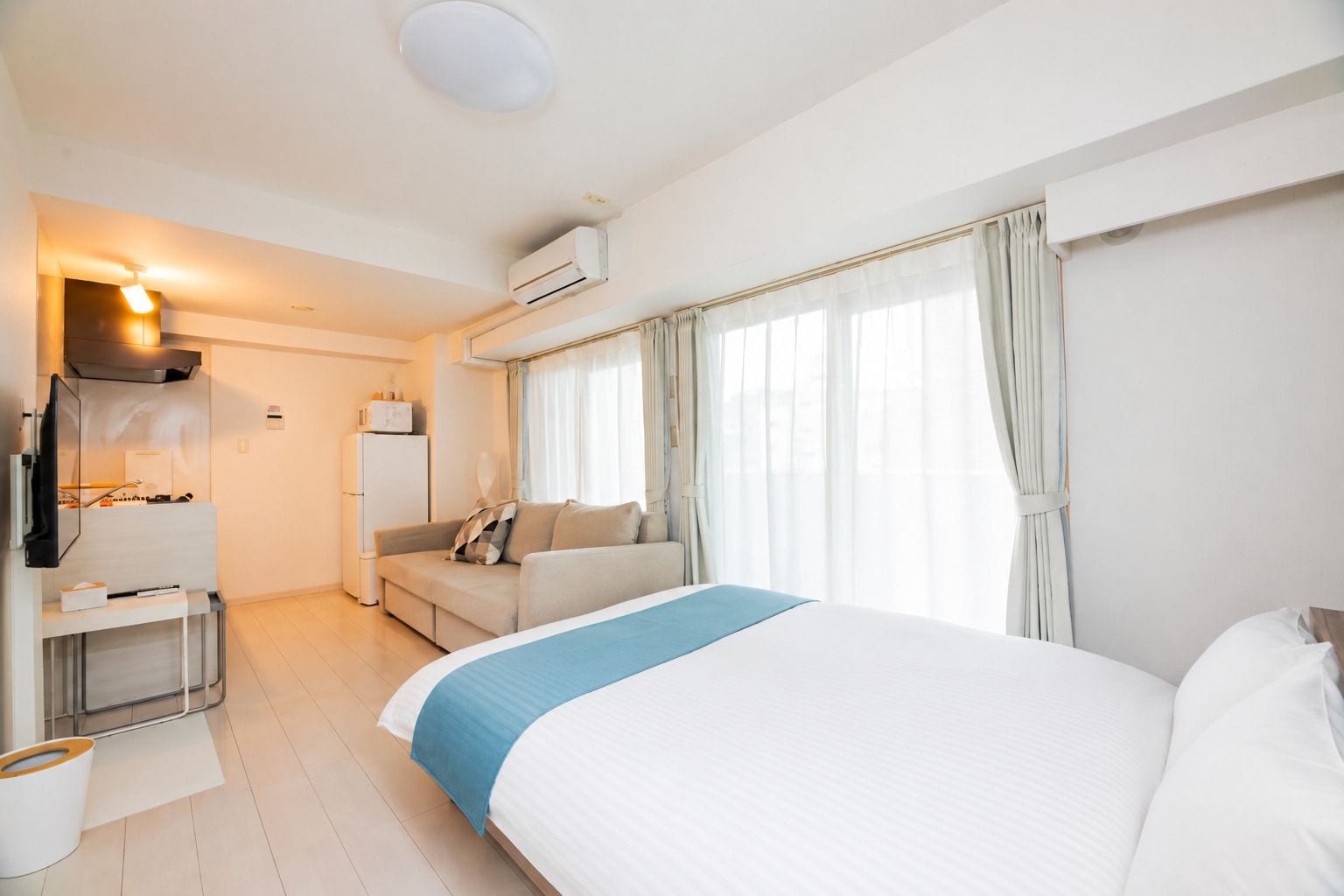 A hotel room with a bed, a sofa, a TV, a desk, and an air conditioning unit.