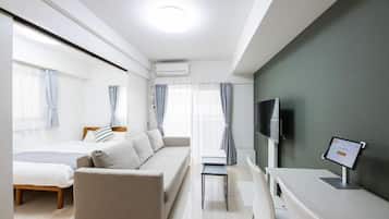 A modern hotel room with a sofa, a bed, a TV, and a desk with a computer.