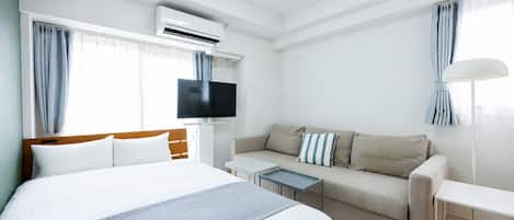 Una habitación de hotel con cama, sofá, televisión y aire acondicionado.