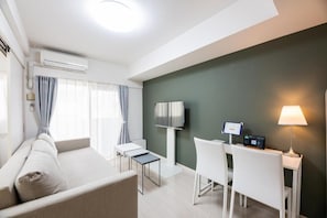 A modern hotel room with a sofa, a small table, a desk with a chair, a flat-screen TV, and a lamp. - Presence Hakata (Fukuoka City Hakata-ku Chiyo)