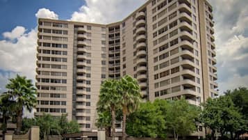 A high-rise building with multiple balconies, surrounded by greenery and palm trees.