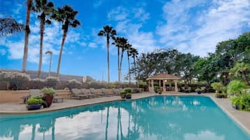 A swimming pool with lounge chairs, palm trees, and a gazebo.