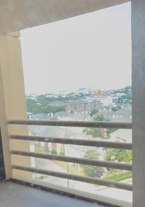 En balkon med gelænder i metal, med udsigt over et boligområde med huse og grønt.