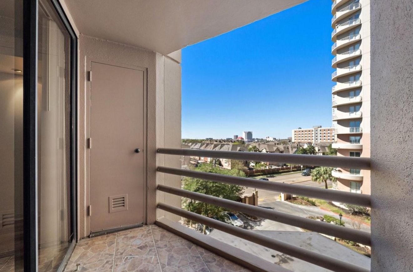 A balcony with a clear view of a cityscape, a door, and a window with blinds.