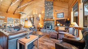A cozy log cabin interior with leather furniture, a stone fireplace, and large windows. - Dancing Bear Lodge, Pine AZ; Luxury Cabin with Views, Spa & Outdoor living area (Pine)