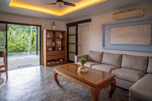 A modern living room with a wooden coffee table, a beige sofa, and a bookshelf. - 3 Bed Jungle View in Bang Por (KBR64) (Koh Samui)