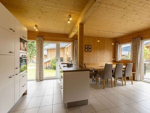 A modern kitchen with a central island, dining area with chairs, and large windows. - One-bedroom Cabin (Sankt Georgen am Kreischberg)
