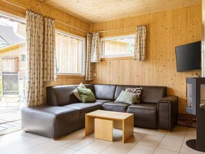 A cozy living room with a sectional sofa, a wooden coffee table, and a flat-screen TV mounted on the wall. - One-bedroom Cabin (Sankt Georgen am Kreischberg)