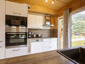 Eine moderne Küche mit Edelstahlgeräten, weißen Schränken und einem großen Fenster mit Blick auf eine gebirgige Landschaft.