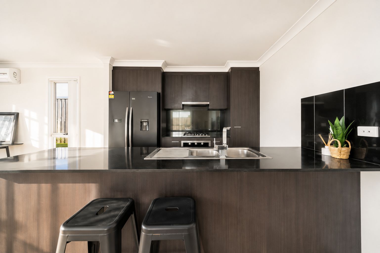A modern kitchen with dark wood cabinets, stainless steel appliances, and a black countertop.