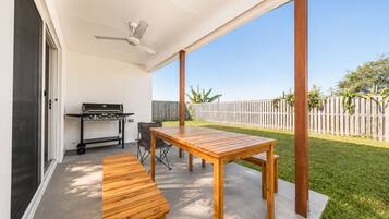 An outdoor patio with a wooden table and benches, a grill, and a ceiling fan.