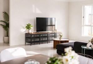 Ein modernes Wohnzimmer mit Flachbildfernseher, einer Couch, einem Couchtisch und einem Topf mit Pflanze.