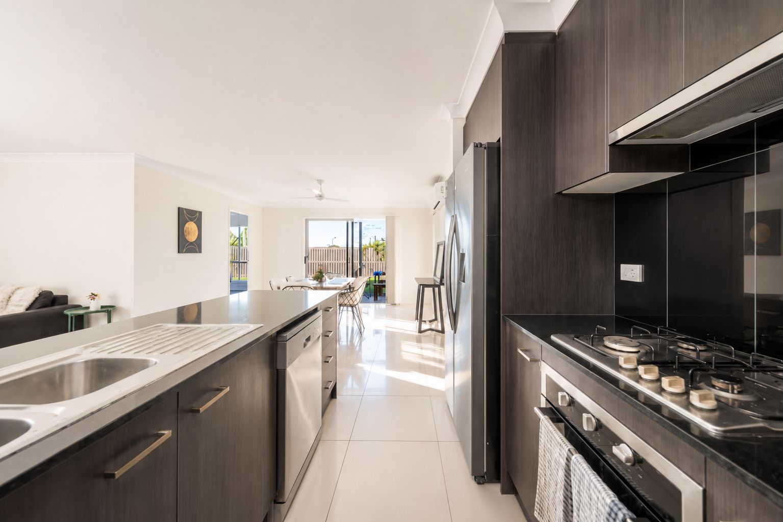 A modern kitchen with dark cabinetry, stainless steel appliances, and a large island with a sink.