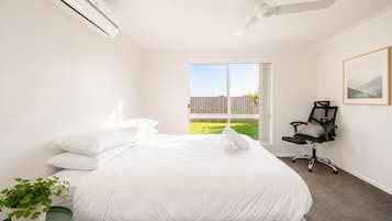 Une chambre à coucher avec un lit, un ventilateur de plafond, une fenêtre, une chaise et une plante.