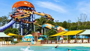A water park with a large water slide, poolside seating, and a tropical backdrop. - The Sunday House - 4B Family Comfort & Style (Pimpama)