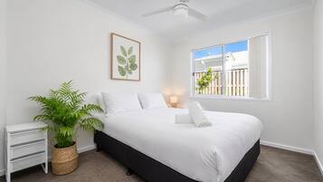A bedroom with a bed, a ceiling fan, a window with a view, a bedside table, and a potted plant.