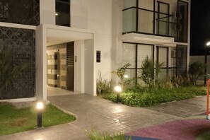 A modern building with a glass entrance, a number '2' sign, and a well-lit pathway with plants. - Your Getaway in Pozos Colorados | Beach and Pools. 10 minutes from the airport. (Santa Marta)