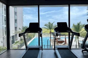 A view from a window with two exercise treadmills facing a swimming pool and a building with balconies. - Your Getaway in Pozos Colorados | Beach and Pools. 10 minutes from the airport. (Santa Marta)