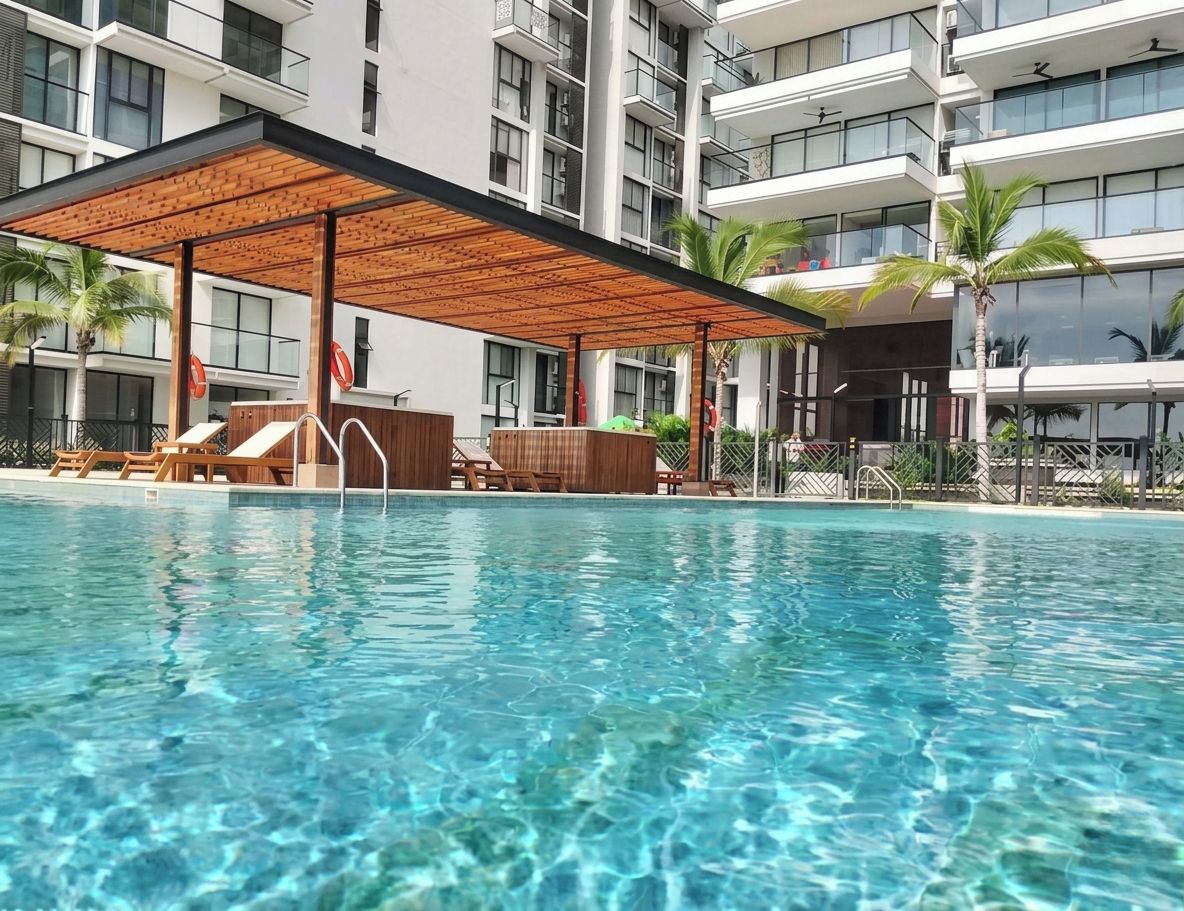 A swimming pool with lounge chairs and a wooden pergola, surrounded by a multi-story building with balconies.