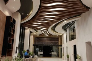 A modern lobby with a curved ceiling, a reception desk, and potted plants. - Your Getaway in Pozos Colorados | Beach and Pools. 10 minutes from the airport. (Santa Marta)