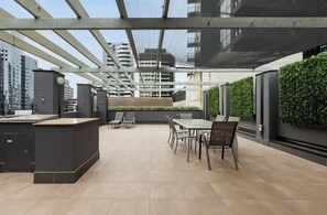 Una terraza en la azotea con zona de comedor, cocina exterior y vistas de los edificios circundantes.