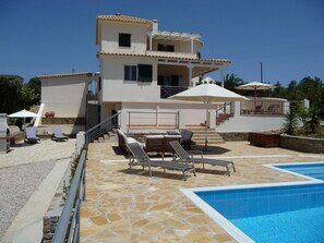 Ein zweigeschossiges Gebäude mit Schwimmbad, Sitzgelegenheiten im Freien und einer Terrasse mit Steinplatten.