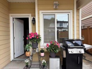 Uma casa com porta da frente, janela, churrasqueira e plantas em vasos.