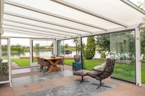 A conservatory with a dining table and chairs, a cushioned seating area, and a view of a lake.