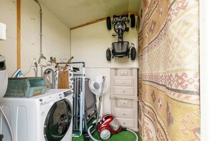 A laundry room with a washing machine, drying rack, ironing board, and a small red toy car.