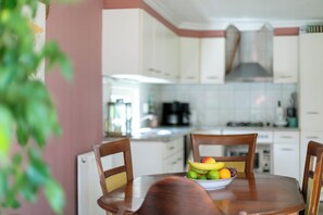 A dining area with a table set for two, a bowl of fruit, and a kitchen in the background.
