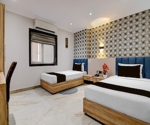 A hotel room with two beds, a desk, a chair, a window with a patterned curtain, and a wall with a geometric design. - Suite Palette Dumdum Airport (Barakpur)