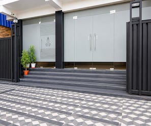 A modern building entrance with a geometric patterned floor, a potted plant, and a metal gate. - Suite Palette Dumdum Airport (Barakpur)