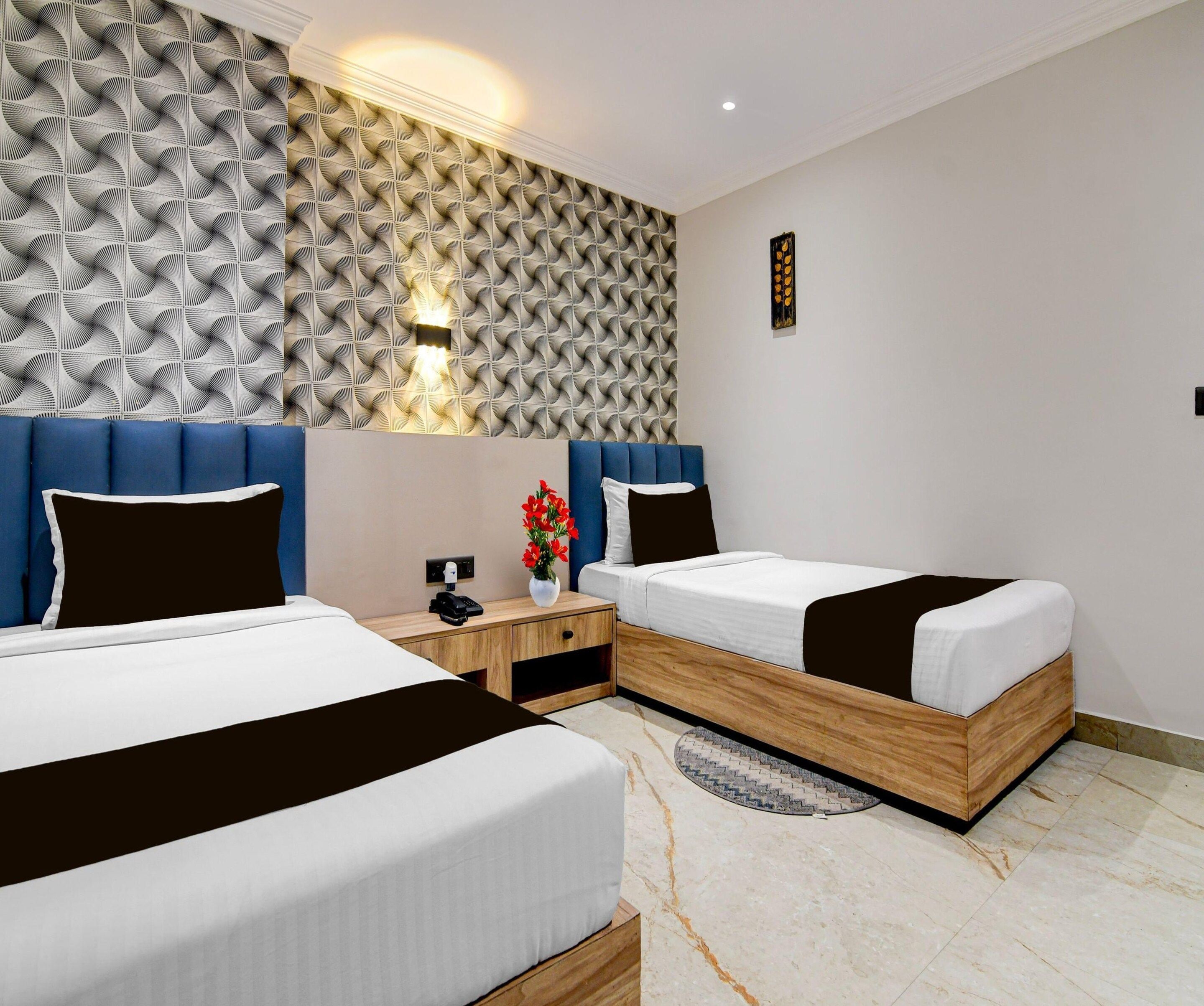 A hotel room with two beds, a nightstand, a wall-mounted light, and a decorative wall panel.