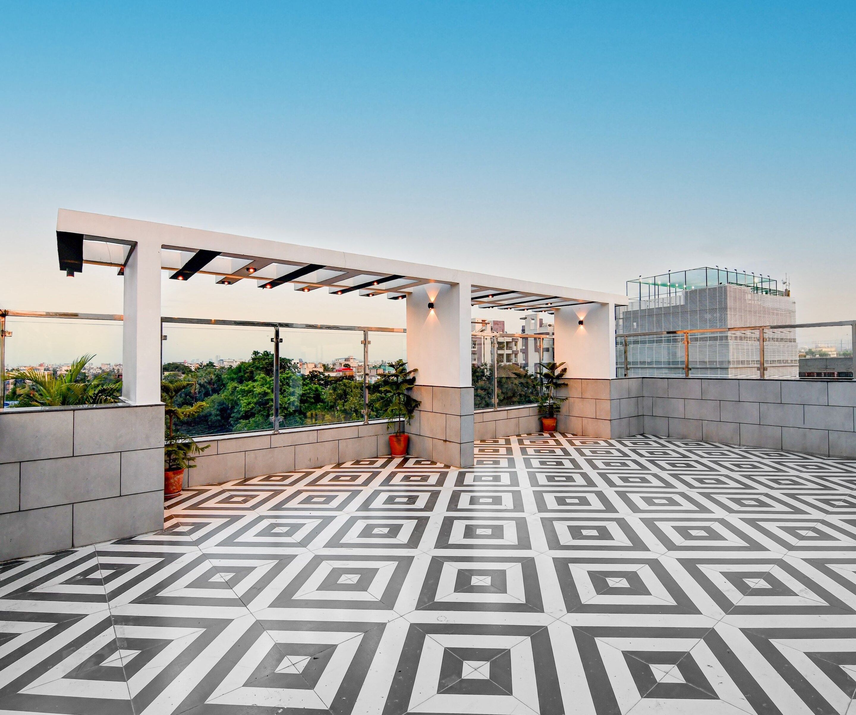 Eine Dachterrasse mit geometrischen Fliesenspuren, einer Pergola-Konstruktion und Topfpflanzen.
