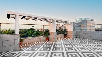 Eine Dachterrasse mit geometrischen Fliesenspuren, einer Pergola-Konstruktion und Topfpflanzen.