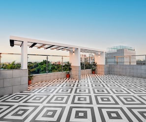 Terrassa al terrat amb paviment de disseny geomètric, una estructura de pergola i plantes en testos.