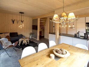A modern interior with a wooden dining table, white chairs, a sofa, and a kitchen area. - Cabin With 1 Bedroom (Sankt Georgen am Kreischberg)