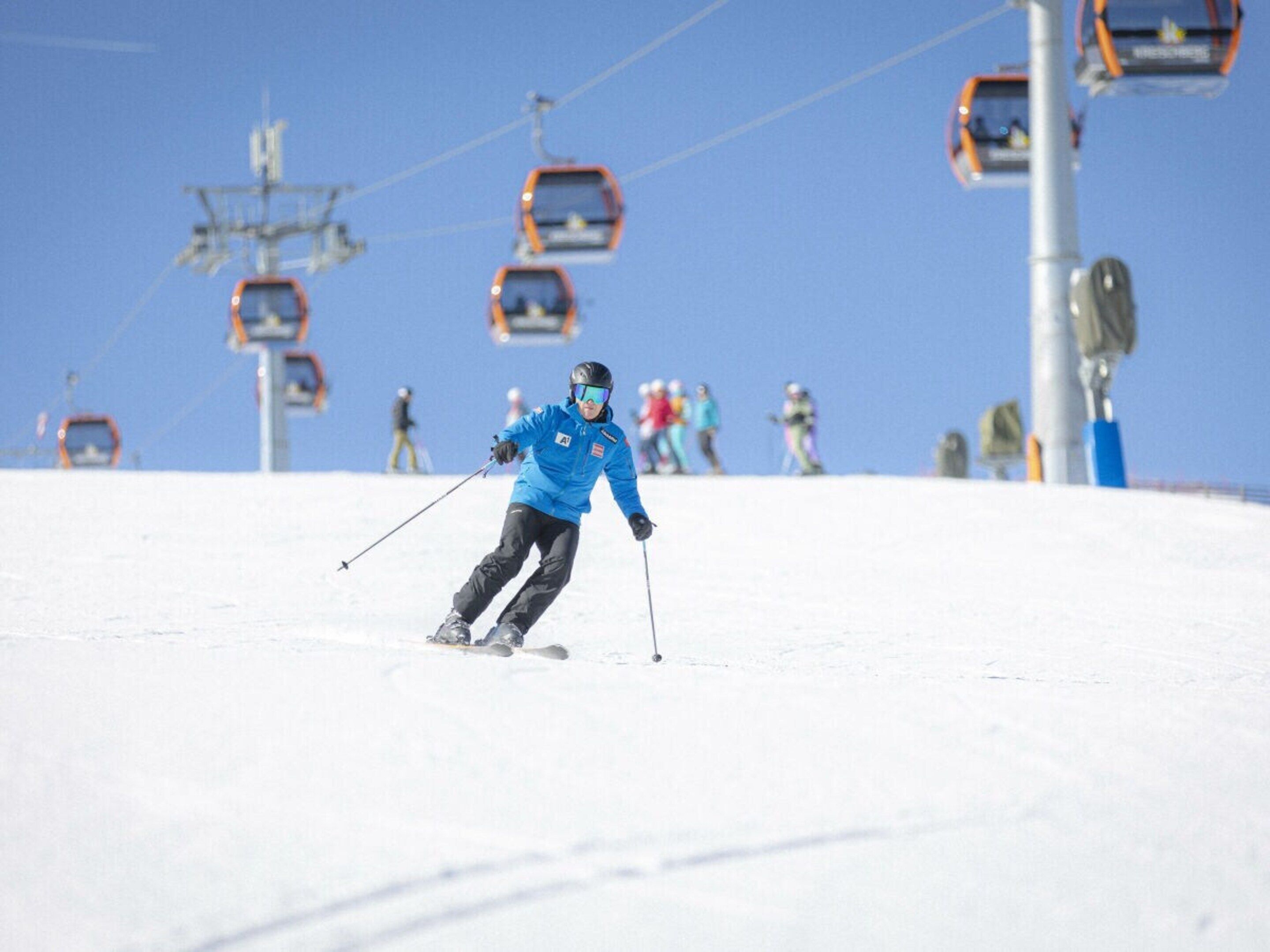 A skier in motion on a snowy slope with ski lifts in the background.