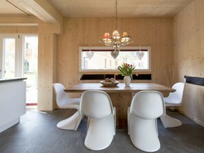 A dining area with a wooden table, white chairs, a vase with flowers, and a chandelier. - Cabin With 1 Bedroom (Sankt Georgen am Kreischberg)