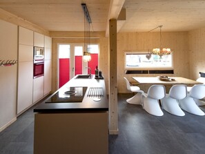 A modern kitchen with a central island, a dining area with white chairs, and a wooden ceiling. - Cabin With 1 Bedroom (Sankt Georgen am Kreischberg)