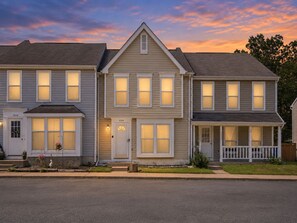 A two-story residential building with a symmetrical facade, multiple windows, and a front porch. - Cozy 3bd townhome - 7 mins to IAD - Free parking + private yard! (Sterling)