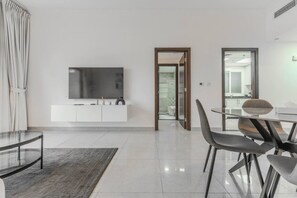 A modern living room with a flat-screen TV, a dining area with a glass table, and a kitchen visible through an open door. - HAVN - 1 Bedroom Apartment in G24 Tower, JVC (Dubai)