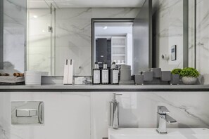 Ein modernes Badezimmer mit Marmorplatte, einem großen Spiegel und einem Waschbecken mit zwei Wasserhähnen.