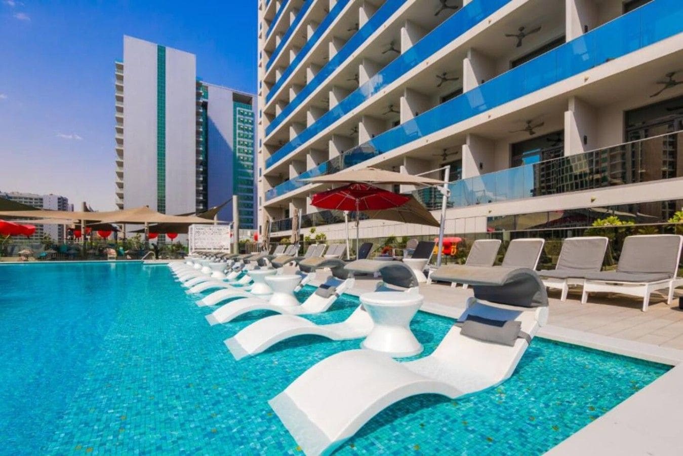 A hotel pool area with sun loungers and umbrellas, surrounded by modern buildings.