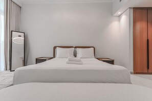 A hotel room with a large bed, a bedside table, a nightstand, a mirror, and a wardrobe. - HAVN - NEW 1 Bedroom in Neva Residences, JVC (Dubai)