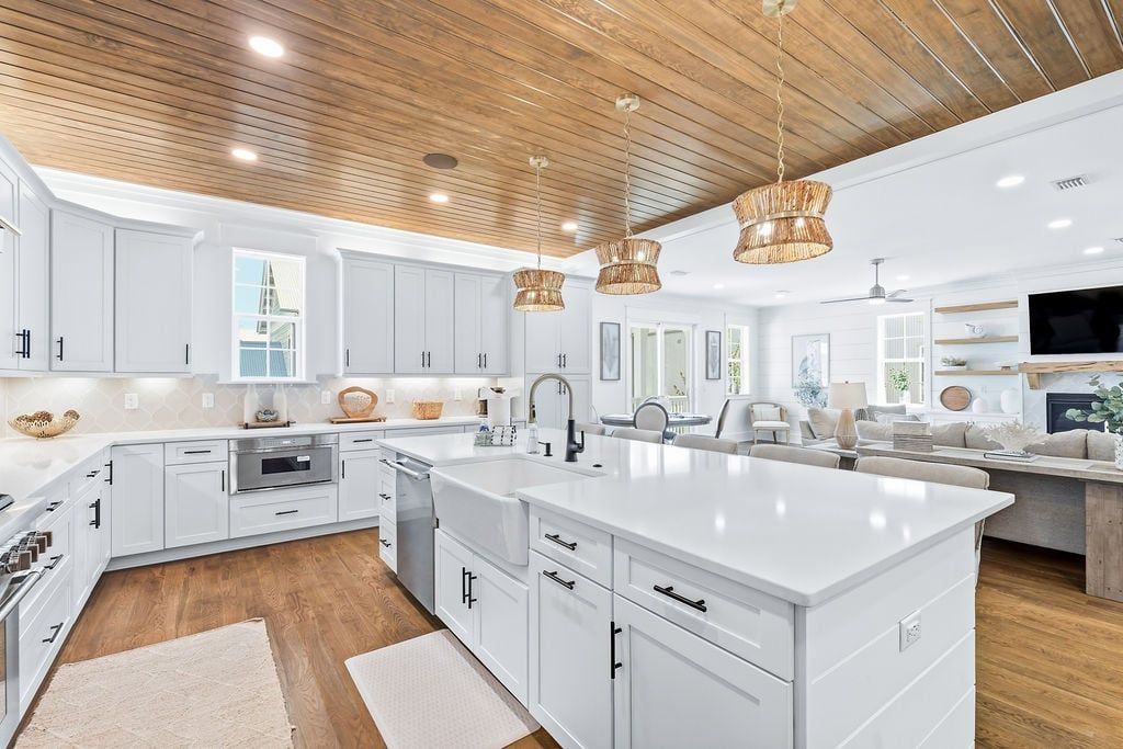 A modern kitchen with white cabinetry, a large island, and wooden ceiling accents.